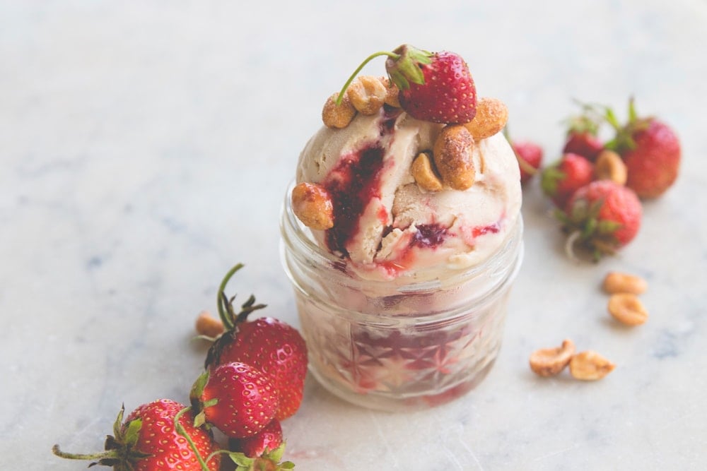 A scoop of ice cream sits in a dish adorned with nuts and strawberries.
