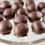 Chocolate-covered peanut butter truffles sit on a glass platter.