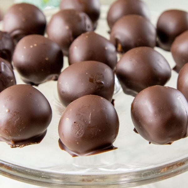 Chocolate-covered peanut butter truffles sit on a glass platter.