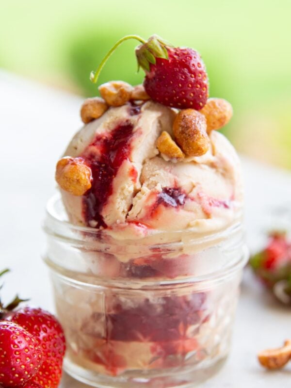 Nuts and a strawberry sit on top of a scoop of ice cream.