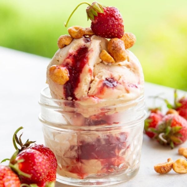 A scoop of ice cream sits in a dish topped with nuts and a strawberry.