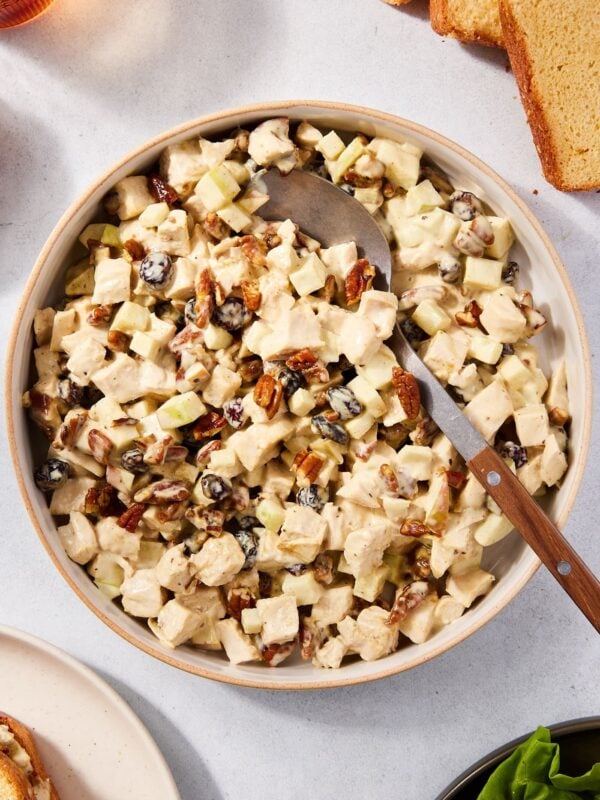 Round bowl filled with apple chicken salad with spoon resting against the side of the bowl all on concrete surface.