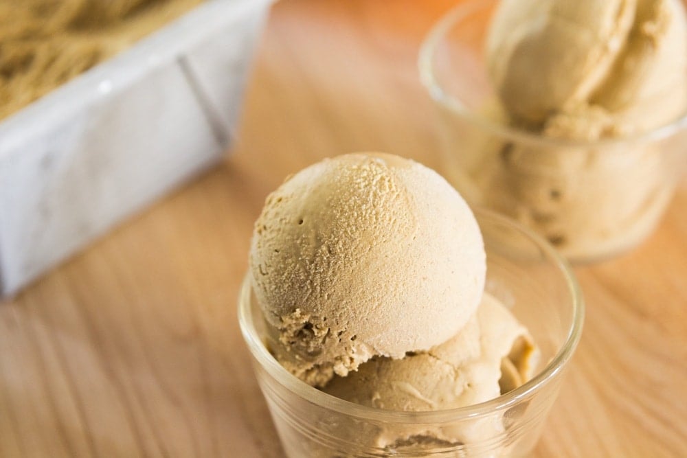 Two scoops of pumpkin ice cream sit in a glass dish.