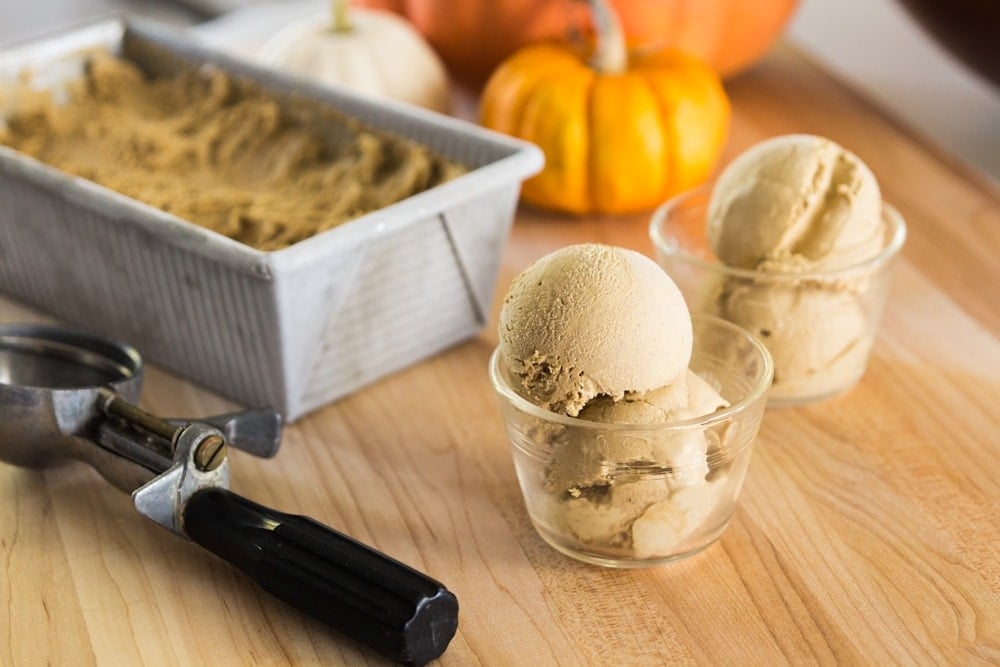 Pumpkin ice cream sits in a dish in from of a larger container and small pumpkins.