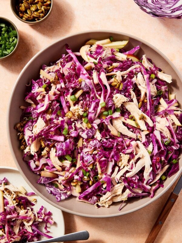 Large bowl filled with ramen chicken salad with purple cabbage with plate filled with serving of the salad.