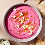 A bowl of beet hummus sits on a table with pita.