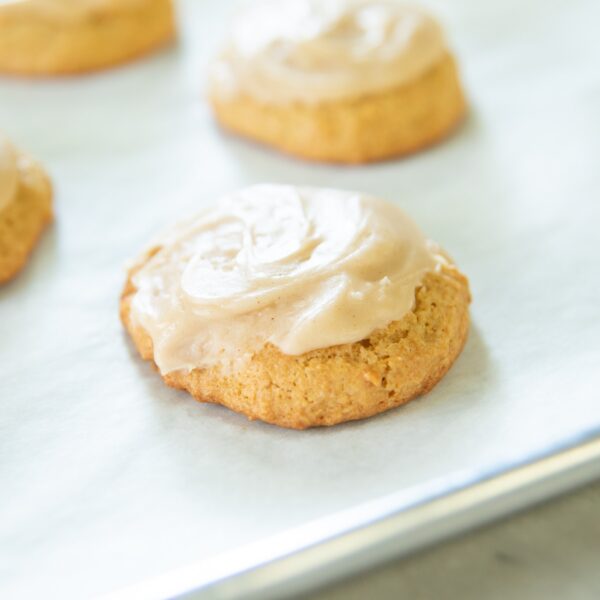 Sugar cookies with frosting sit on a parchment-lined pan.