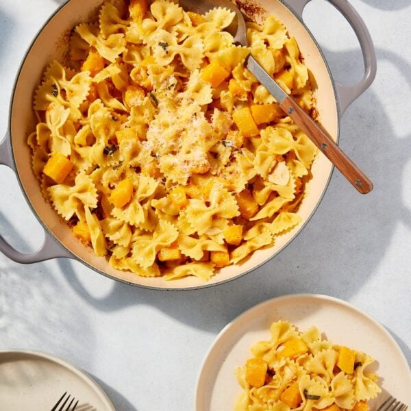 Large pot filled with cooked browned butter squash pasta with serving on a white plate with spoon resting against the side of the pot.