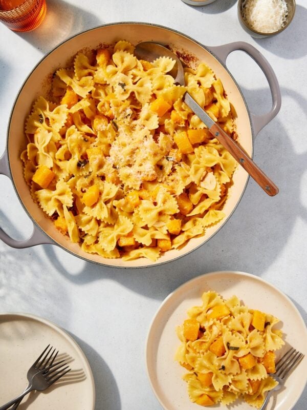 Large pot filled with cooked browned butter squash pasta with serving on a white plate with spoon resting against the side of the pot.
