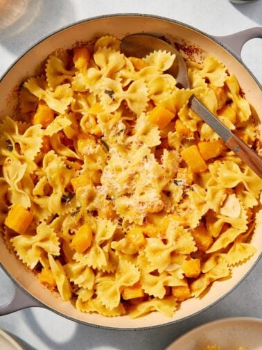 Large pot filled with cooked browned butter squash pasta with Parmesan cheese sprinkled over top with spoon about to scoop out another serving.