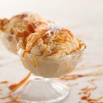 Two scoops of caramel ice cream sit in a glass dish.