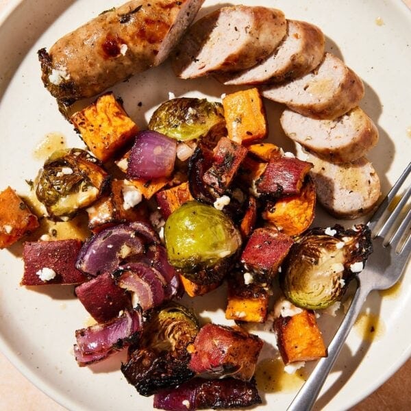 White plate filled with sliced pieces of sausage and roasted vegetables drizzled with homemade vinaigrette.