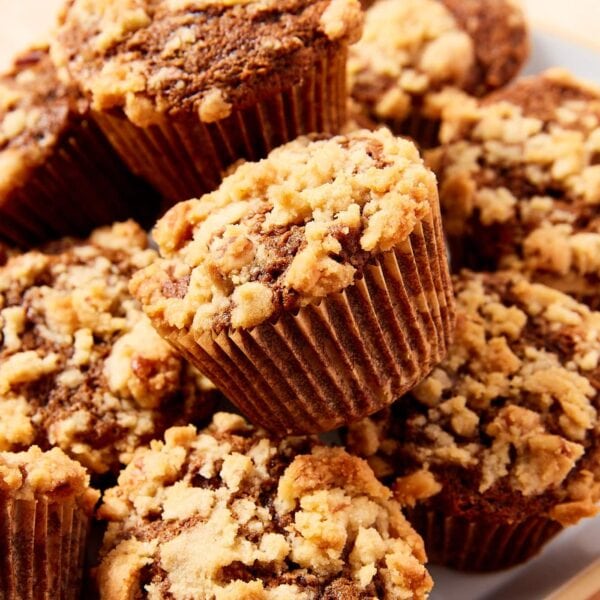 Pile of baked carrot muffins resting on white plate with muffin papers still on.