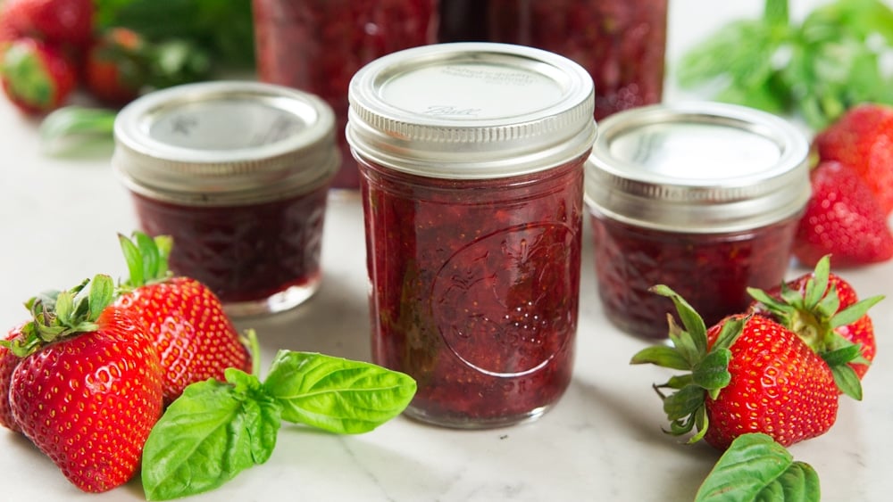A jar with strawberry basil preserves sits on a table.