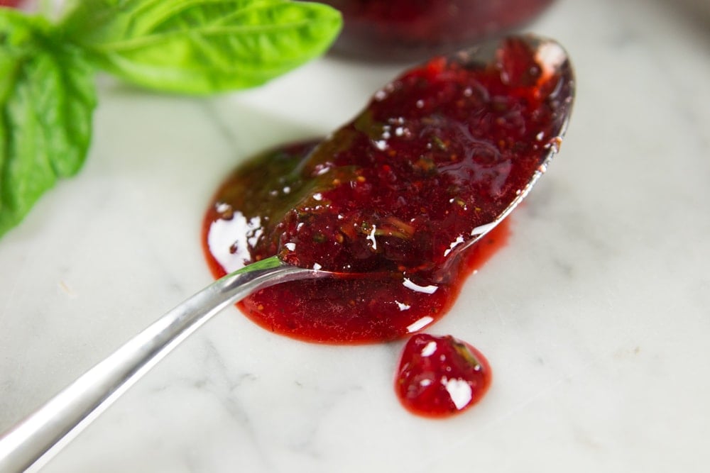 Strawberry basil preserves spill off a spoon onto a table.