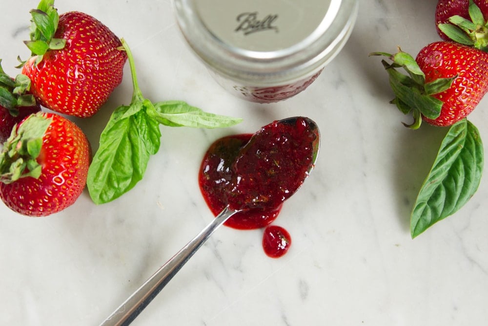 A spoon with strawberry preserves on a table.