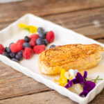 French toast accompanied by berries and flowers sits on a plate.