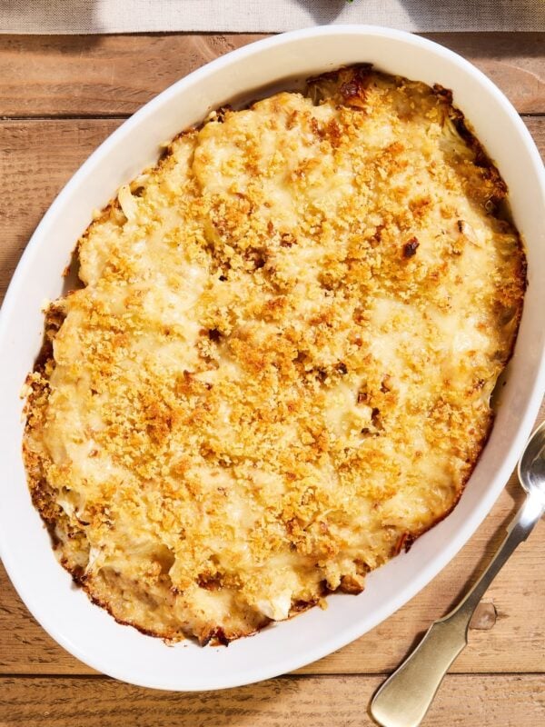 Wood table with white baking dish filled with cauliflower au gratin topped with fresh breadcrumbs after coming out of the oven.