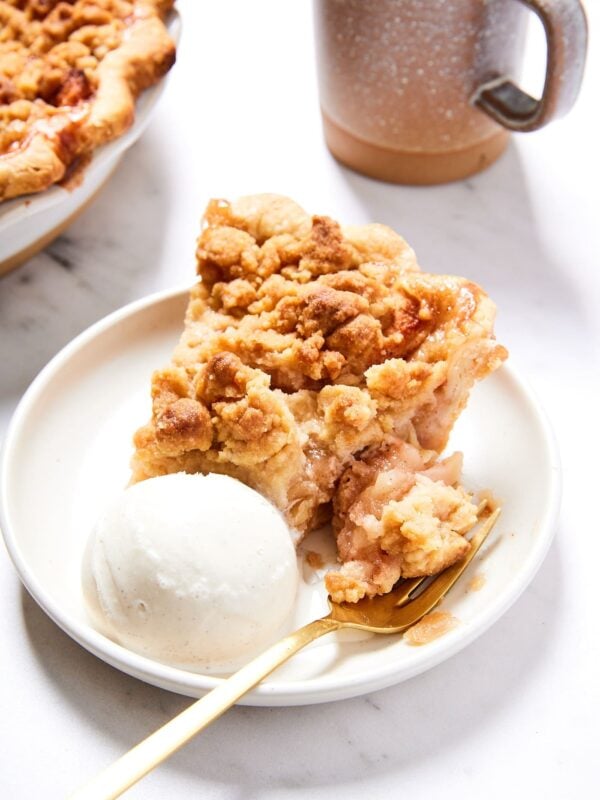 White plate with slice of classic apple with bite taken out and resting on a fork along with a scoop of ice cream.