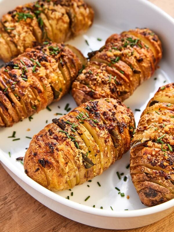 White baking dish filled with baked Hasselback potatoes with fresh chives sprinkled on top and garlic butter topping.