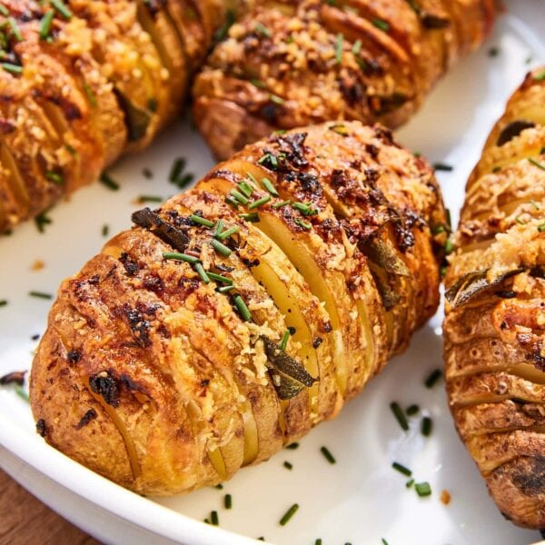 White baking dish filled with Hasselback potatoes with garlic butter topping with pieces of chopped fresh chives all around.