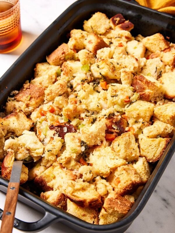 Large black rectangular baking pan filled with baked traditional stuffing with lots of cubes of bread all on white marble surface.