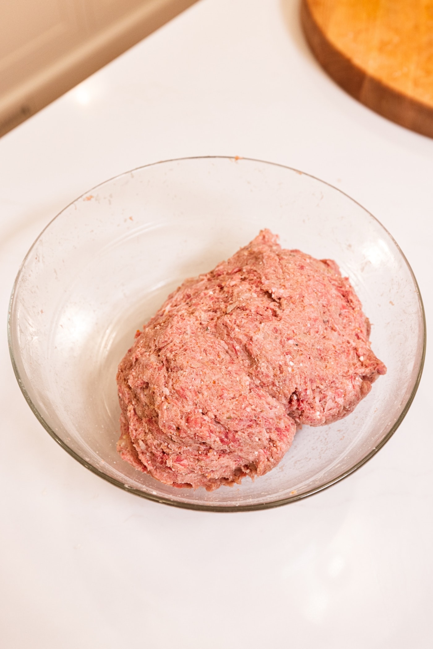 Ball of meatball mixture mixed together in a glass bowl sitting on a white surface.