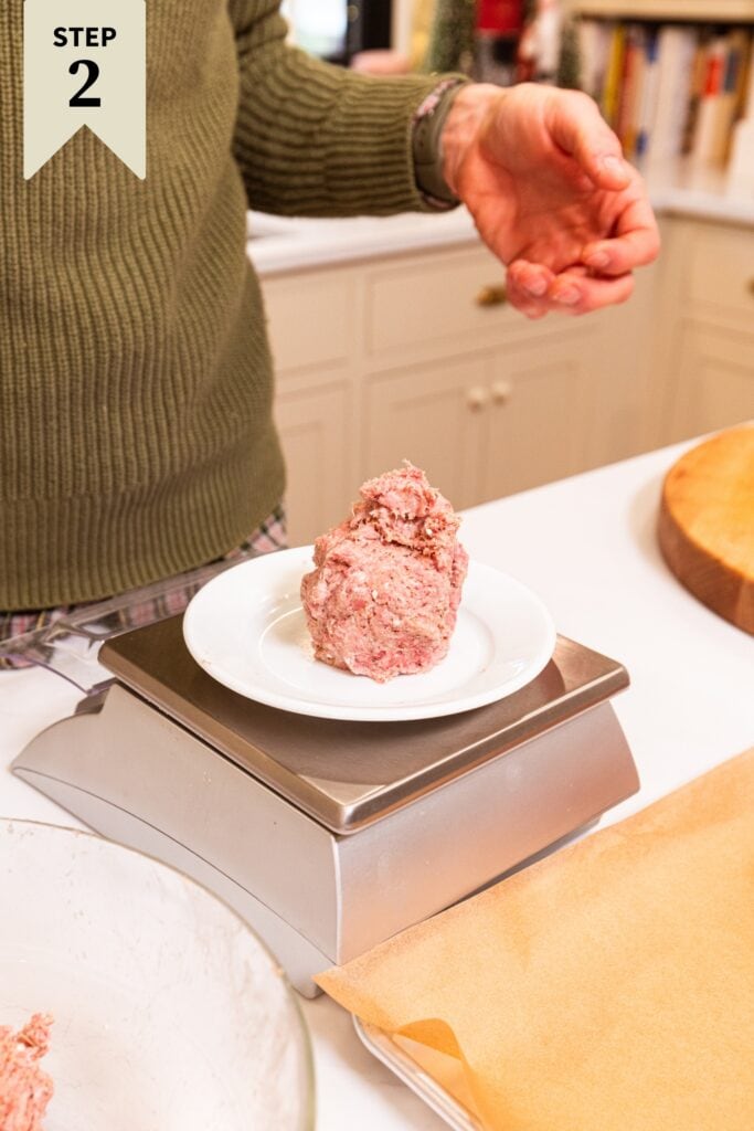 White plate sitting on a food scale with ball of meat on top measuring the size for a meatball.