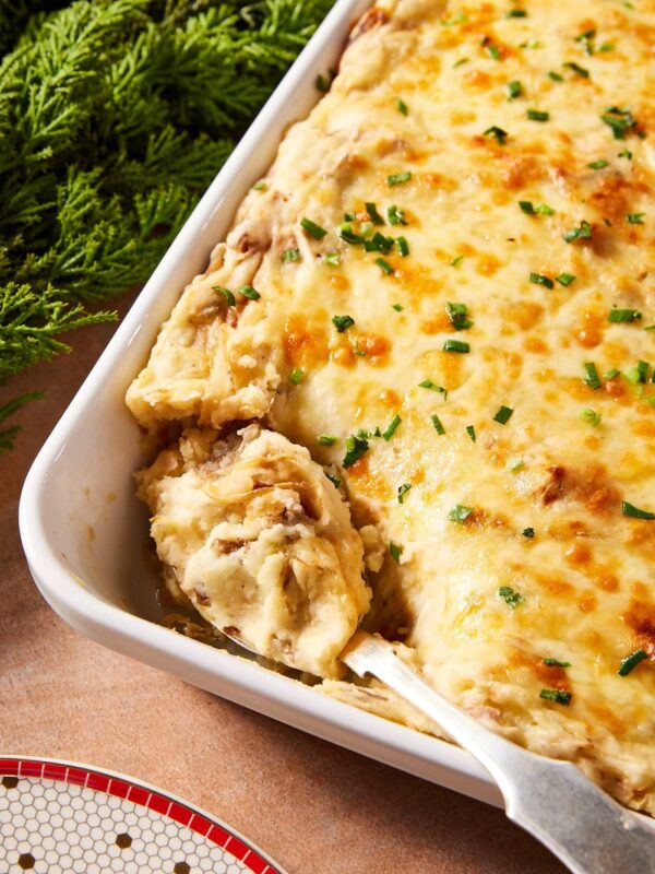 White baking dish filled with French onion potato casserole with cheese-covered topping with spoon scooping out a serving.