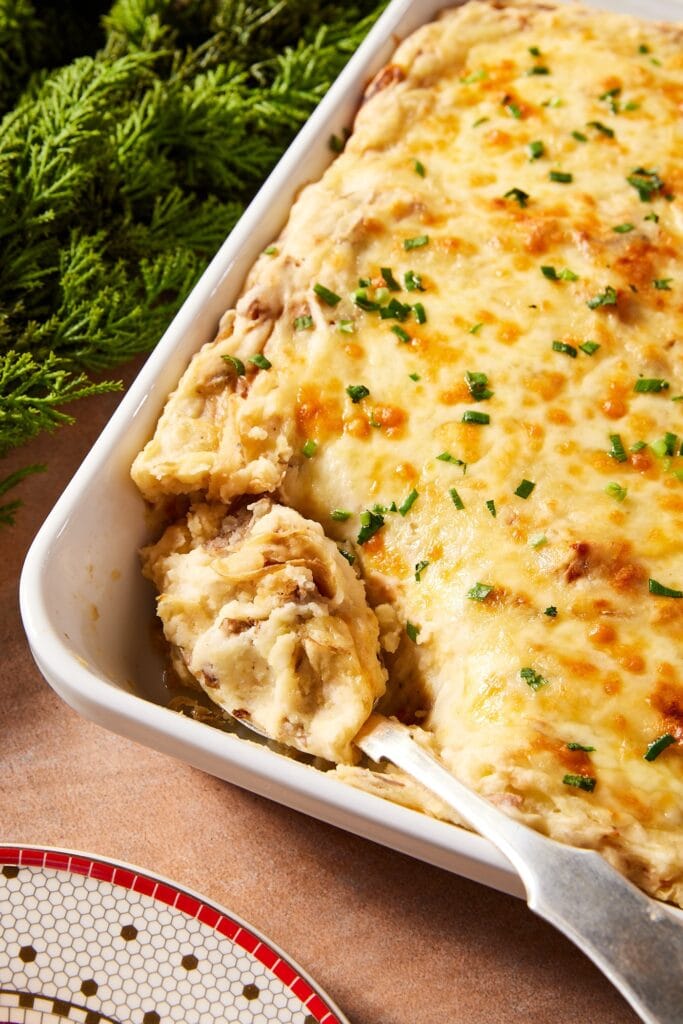 White baking dish filled with French onion potato casserole with cheese-covered topping with spoon scooping out a serving.
