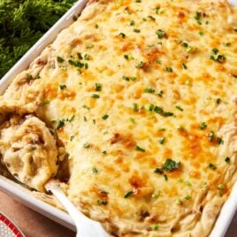 Large white baking dish filled with French onion potato casserole with cheese over the top and sprinkled with chopped parsley.