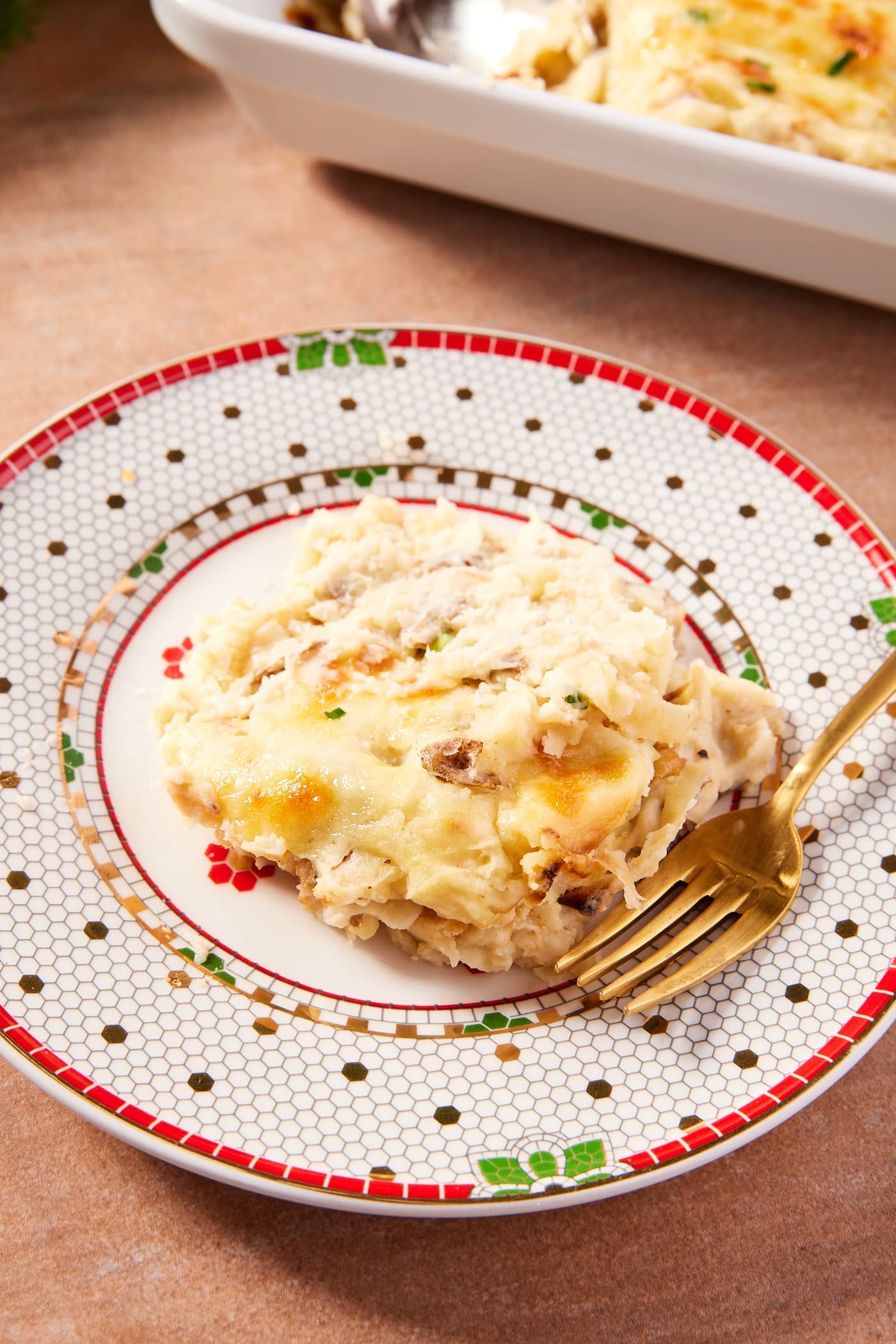 Holiday plate with serving of French onion potato casserole with gold fork showing cheesy texture.