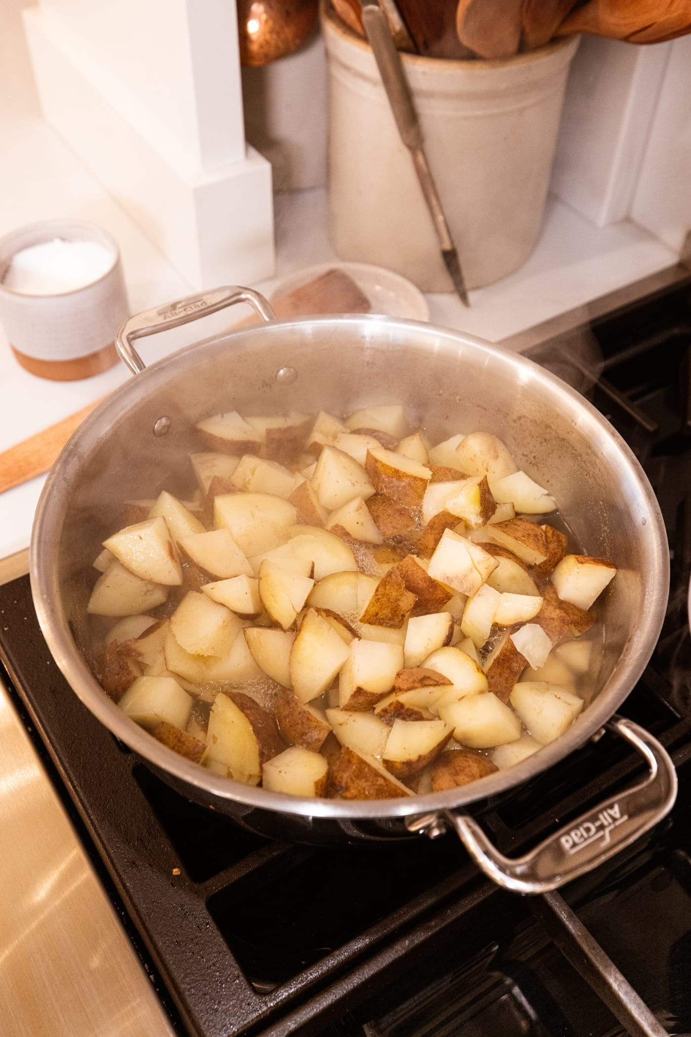 Metal stockpot on stove with steam rising off the top of cubed cooking potatoes.
