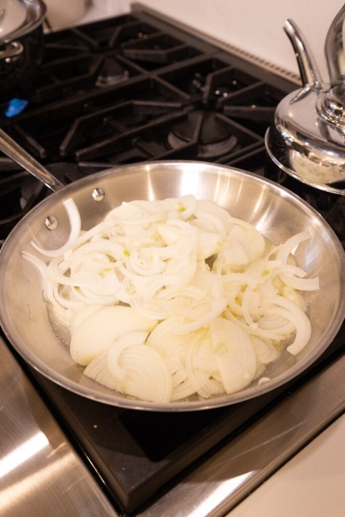 Slices of onion in a metal skillet at the beginning of caramelization process.