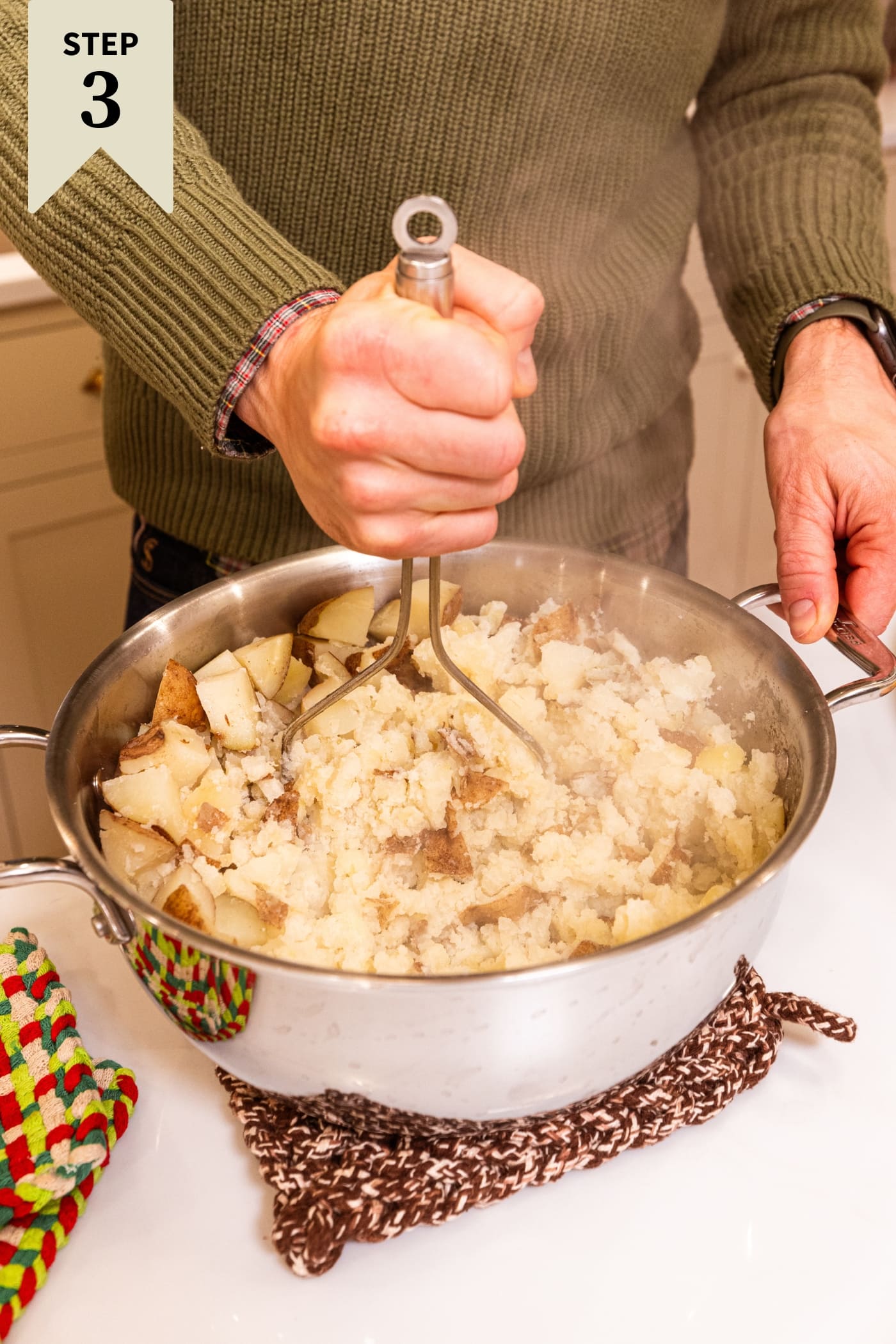 Hand holding potato masher mashing potatoes together in a large stockpot.