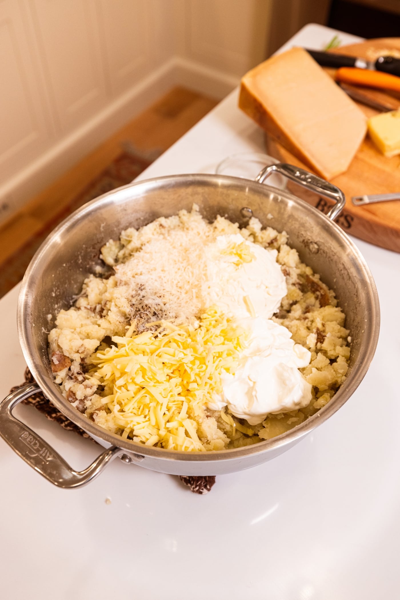 Mashed potatoes in large stockpot with cheese, sour cream, and cream cheese on top.