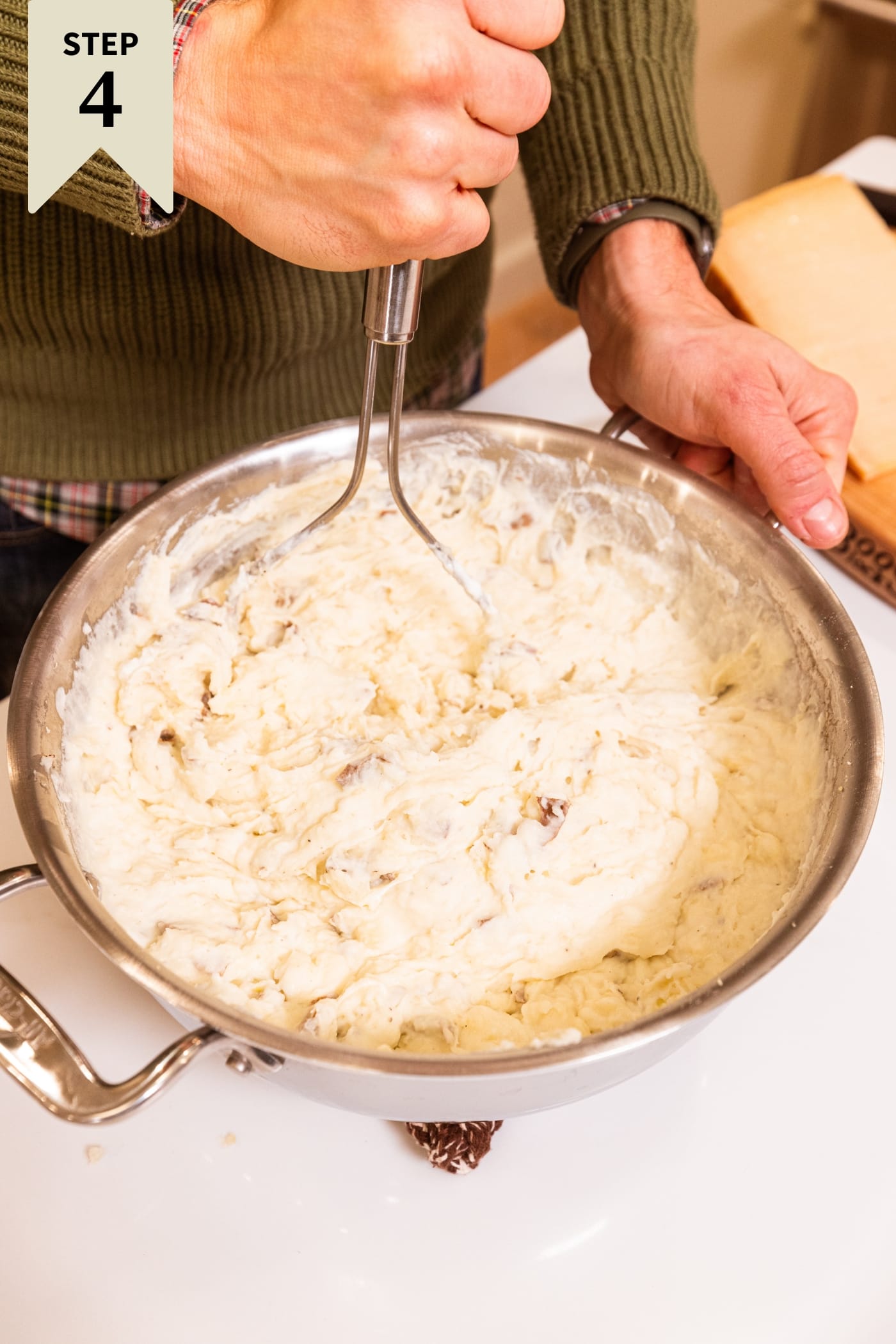 Hand holding potato mashed showing mashed potato mixture after adding cheese.