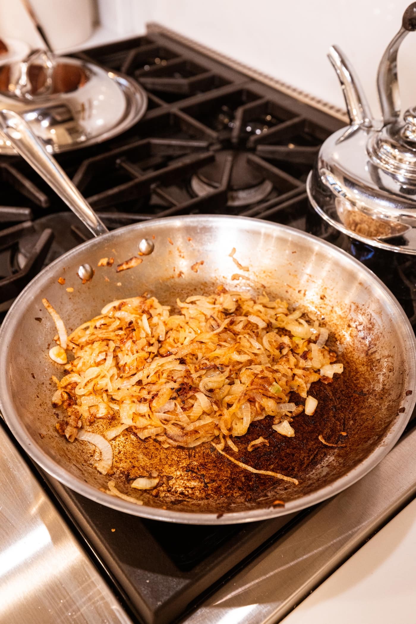 Caramelized onions in metal skillet on stovetop with fond on the bottom of pan.