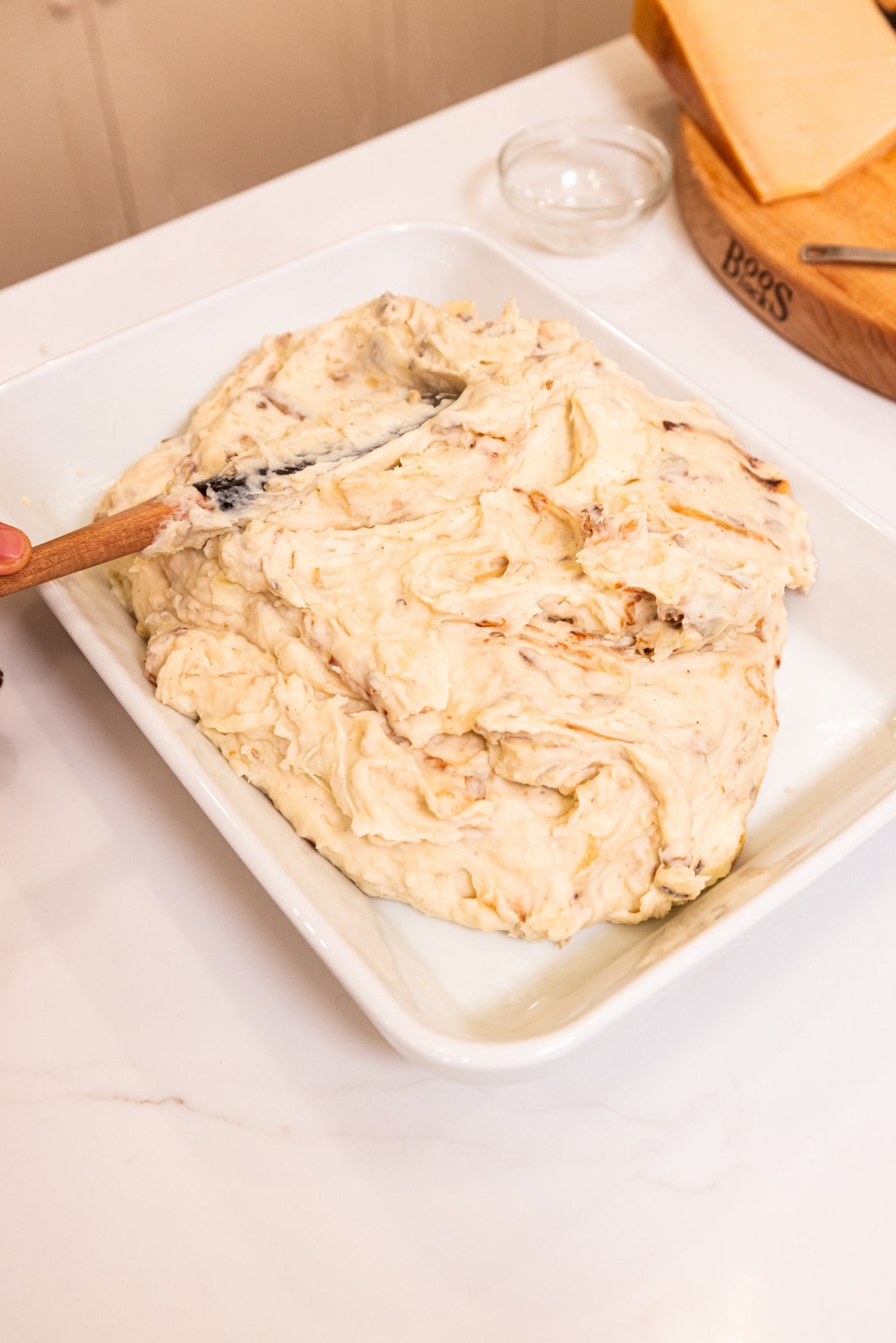 Large white baking dish filled with French onion potato mixture with offset spatula smoothing it out to an even layer.