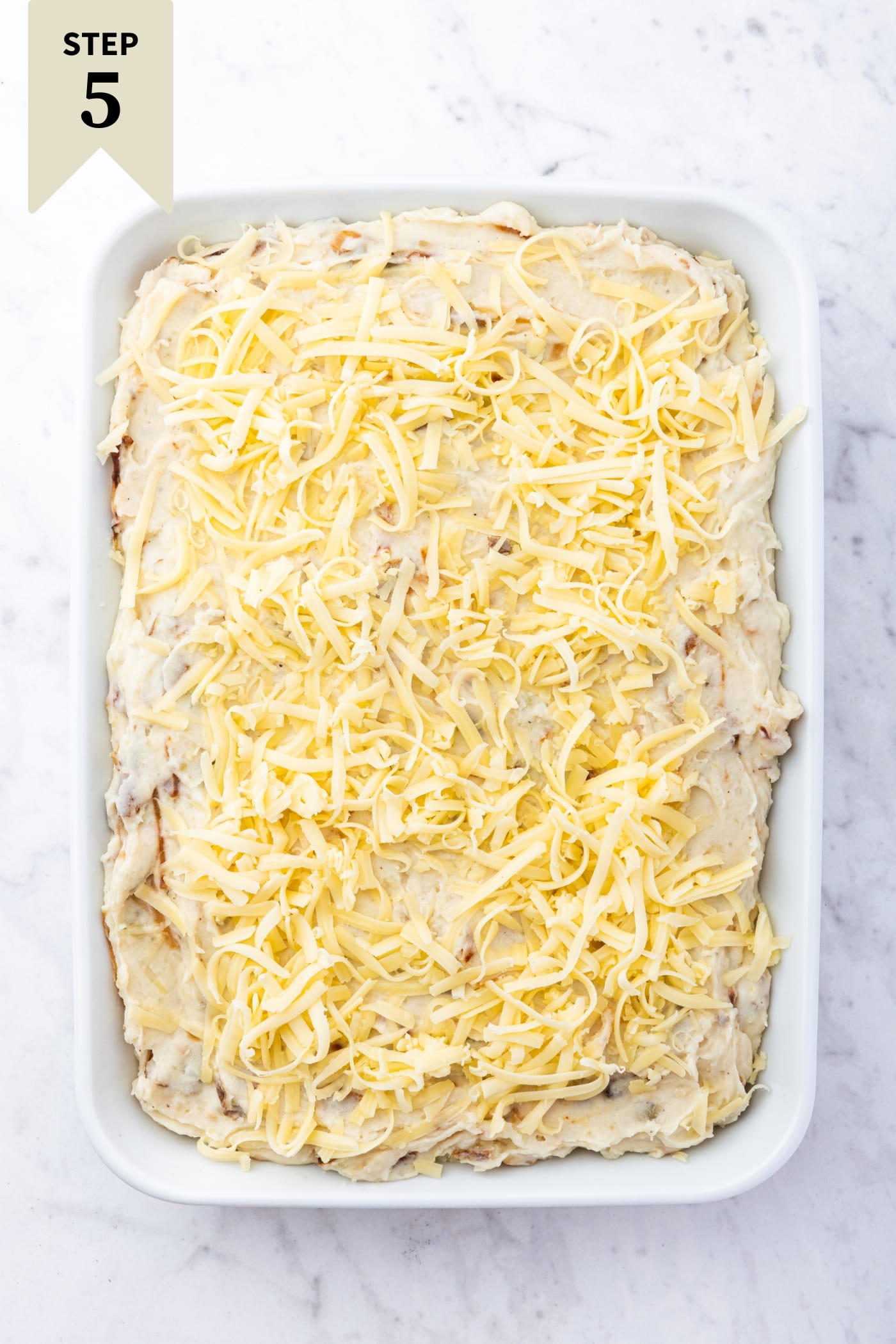 White marble surface with white baking dish filled with unbaked French onion potato casserole