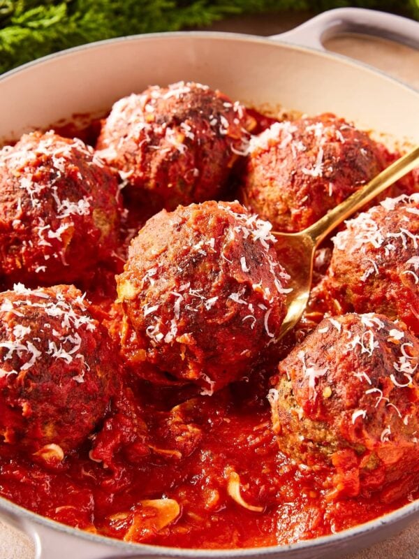 Tomato sauce covered meatballs sitting in round baking dish with gold spoon picking up one meatball.