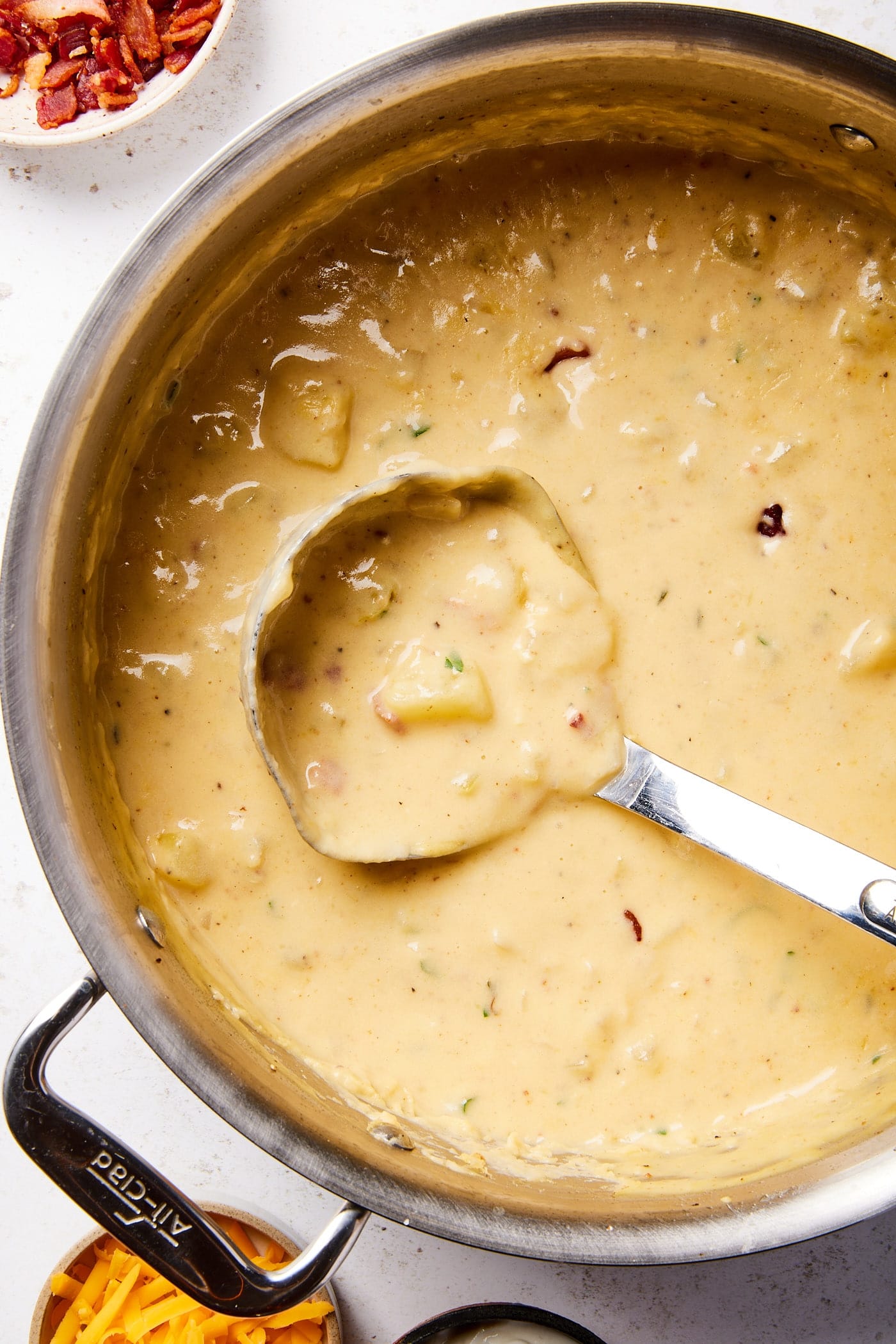Large metal stockpot filled with taupe colored baked potato soup with ladle resting against the side.