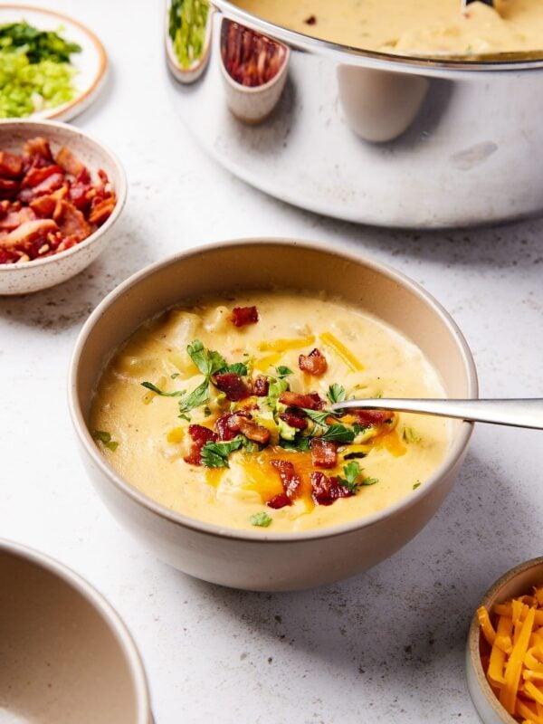 Brown bowl filled with loaded baked potato soup with bacon and cheese on top with spoon resting on side of bowl.