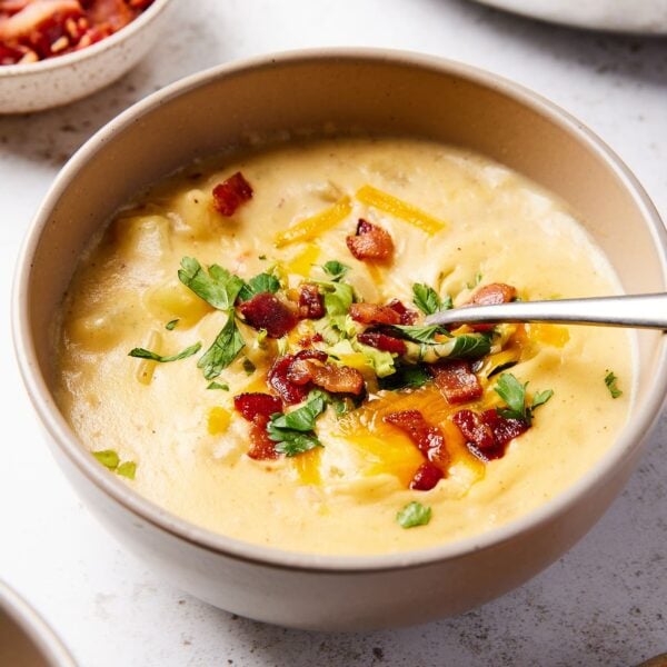 Bowl filled with serving of baked potato soup with spoon in bowl and sprinkled with bacon and cheese.