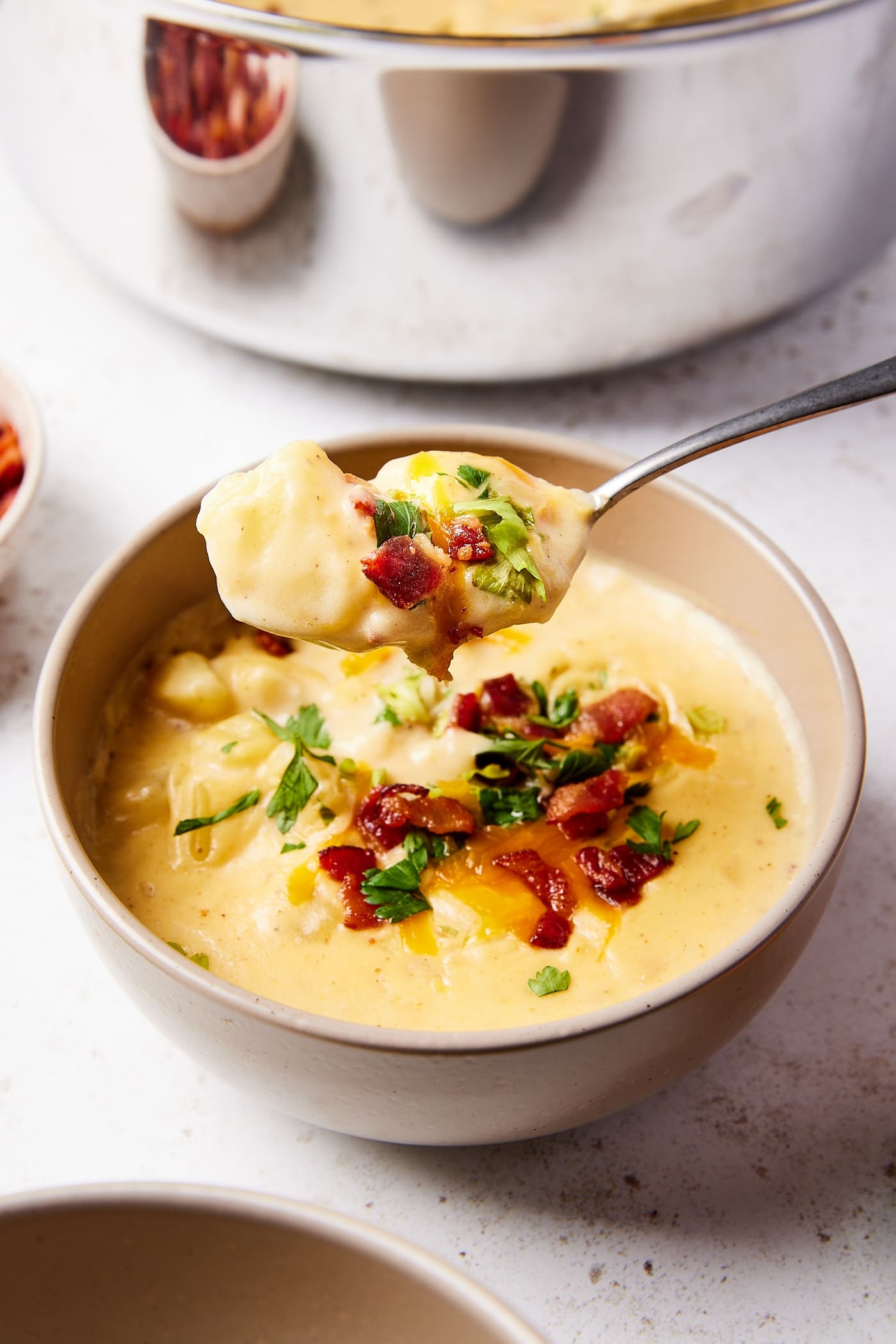 Brown bowl filled with baked potato soup with bacon and cheese sprinkled on top with spoon pulling out a serving.
