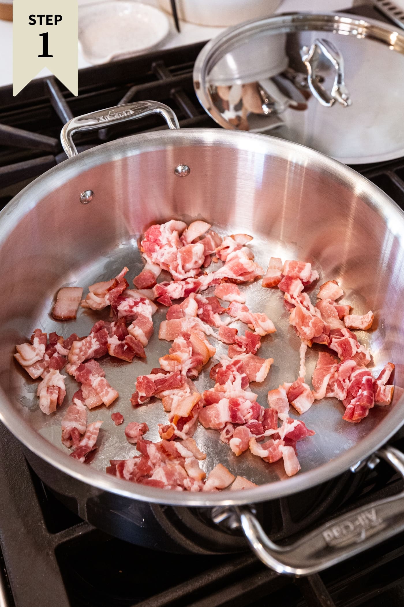 Large metal pan filled with uncooked bacon in oil ready to be cooked until browned.