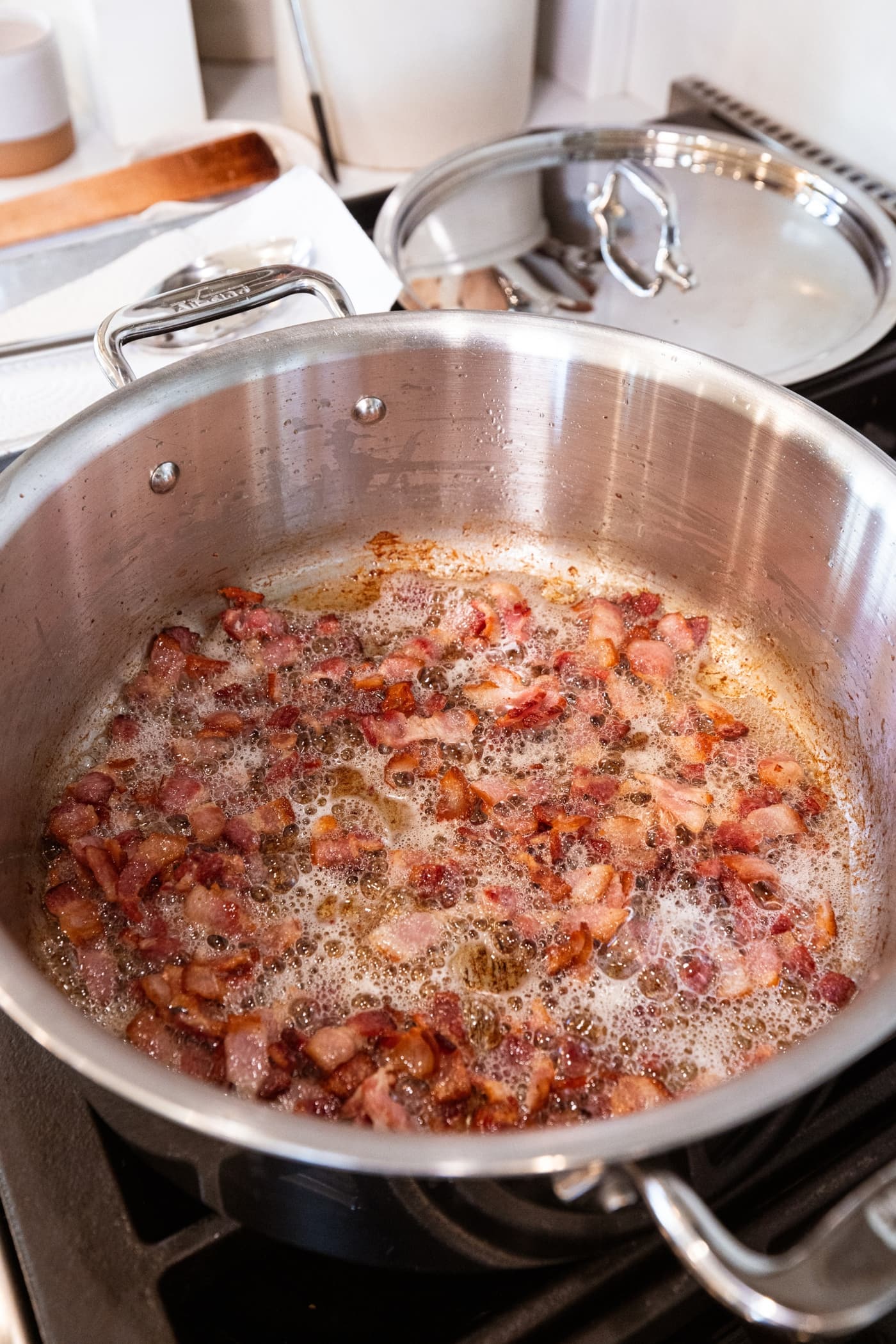 Large metal pot filled with cooking bacon pieces with bubbles all around from the fat.