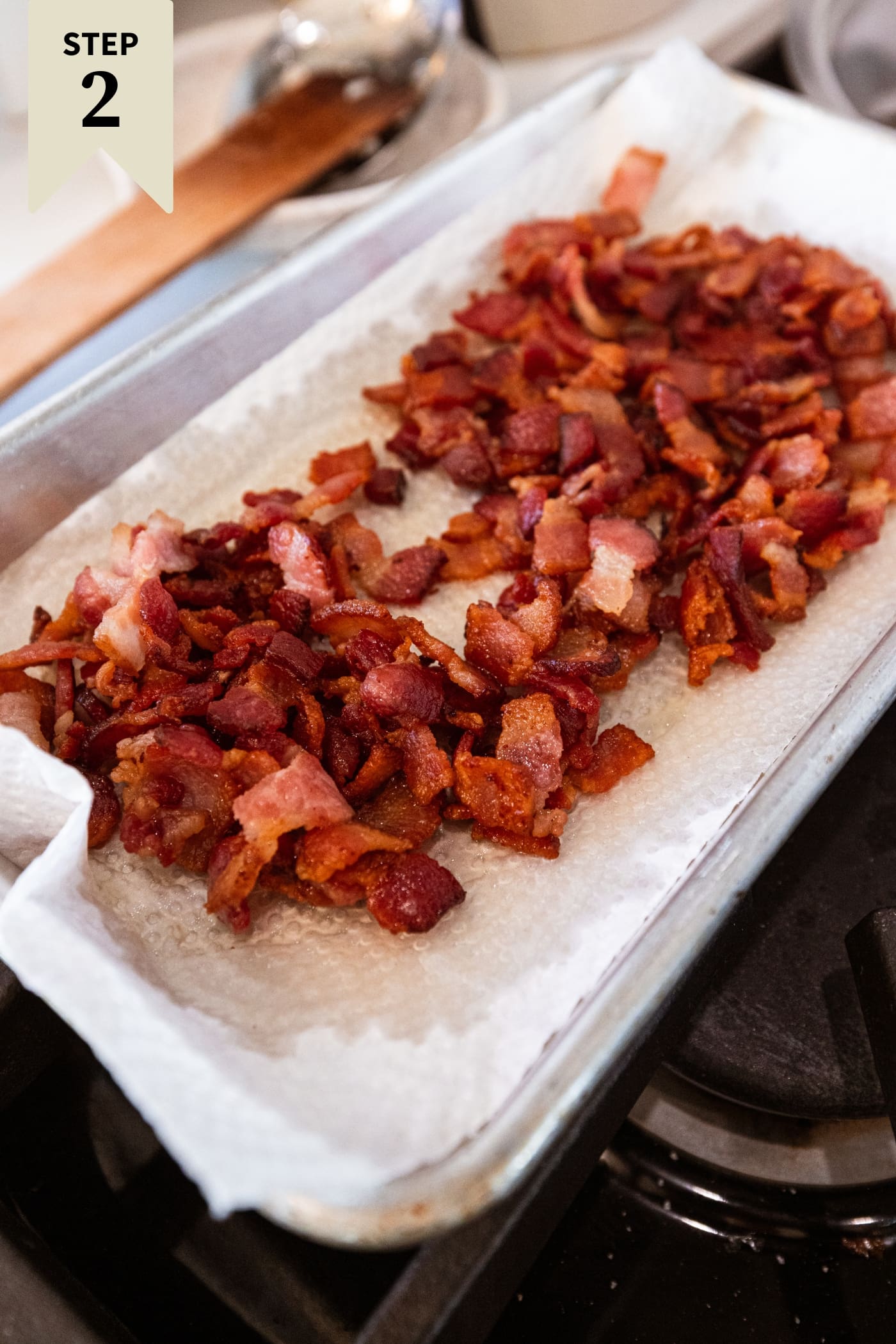 Cooked bacon resting on a paper towel-lined small pan after being cooked on the heat on the stove.