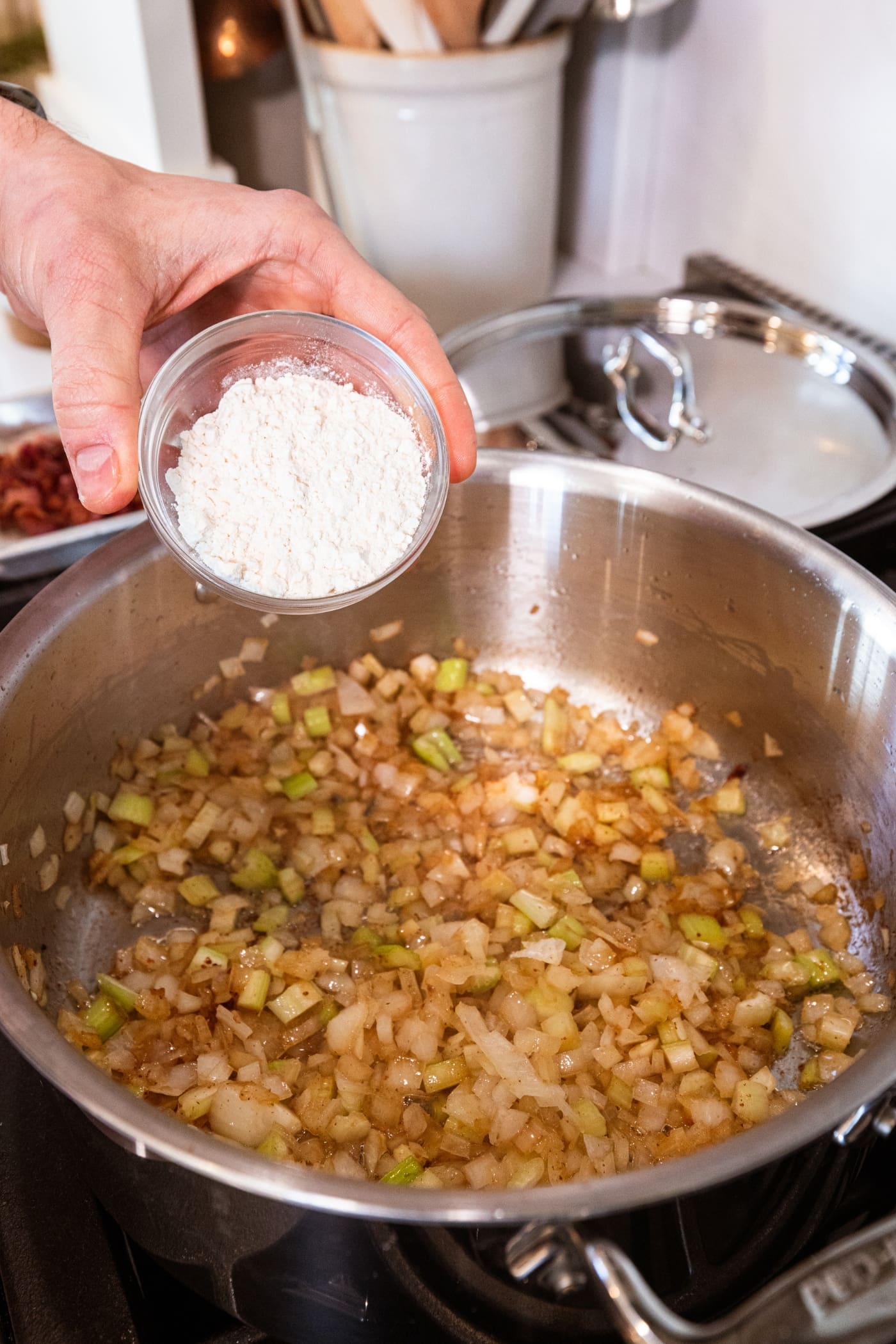Hand about to pour flour into a large stockpot filled with cooked onions and celery.