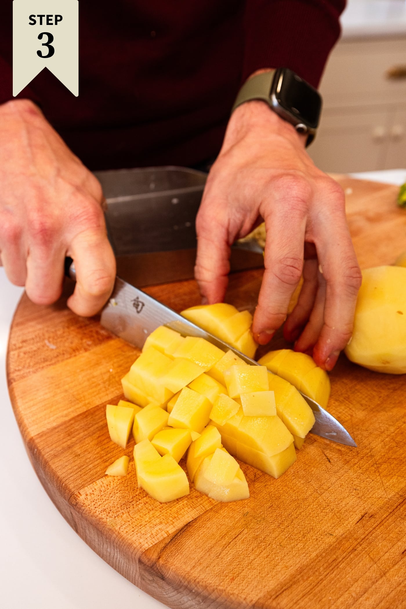 Hand using knife to slice potato into chunks before adding to a potato soup.